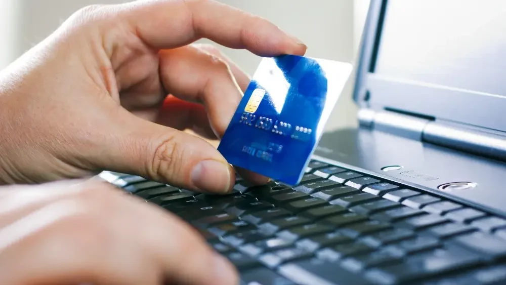 Main tenant une carte de crédit près d'un ordinateur.