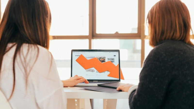 Deux personnes examinent des données d'un site web sur un ordinateur portable, tandis qu'une flèche descendante illustre une baisse.