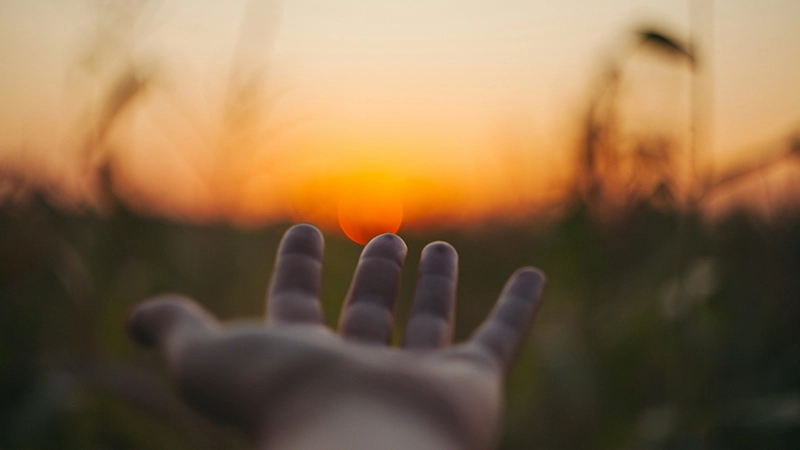 Hand reaching toward the setting sun